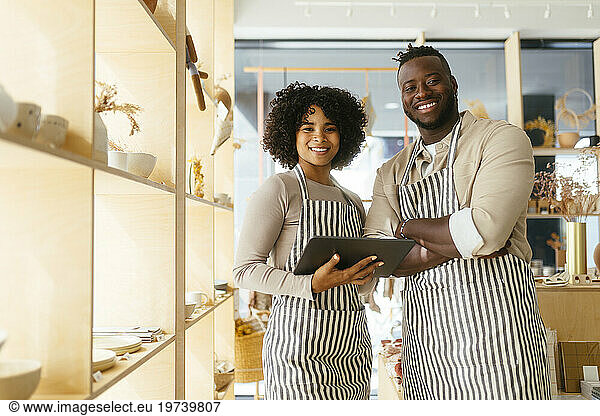 Smiling owners holding tablet PC and standing at store