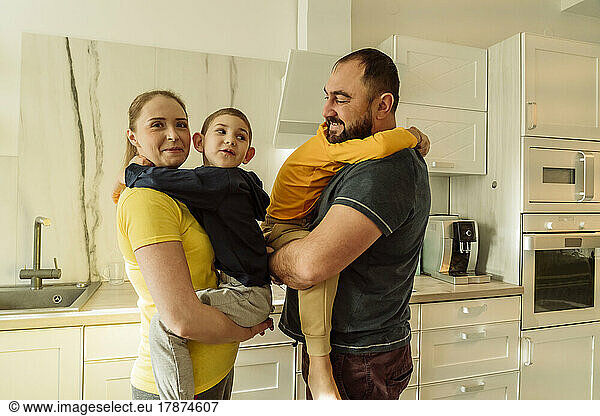 Smiling parents carrying sons in kitchen