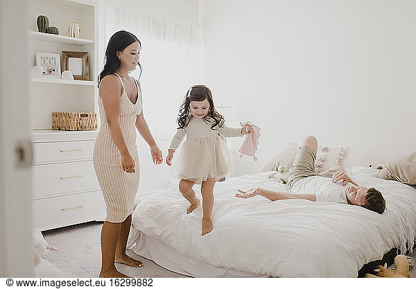 Smiling parents looking at daughter standing on bed at home