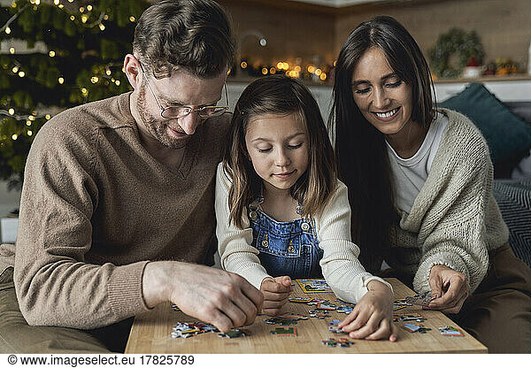 Smiling parents with daughter joining puzzle at home