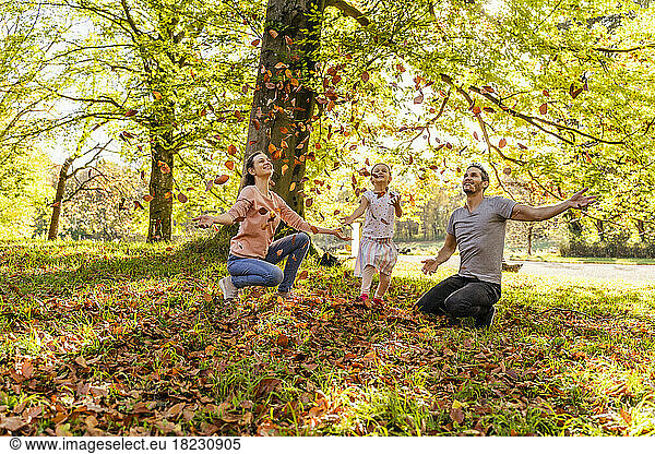 Smiling parents with daughter throwing autumn leaves in park