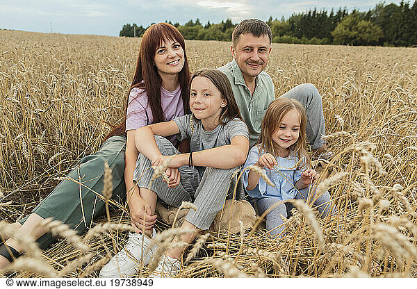Smiling parents with daughters sitting amidst field