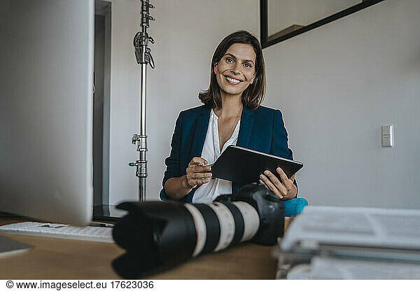 Smiling photographer with tablet PC sitting in studio