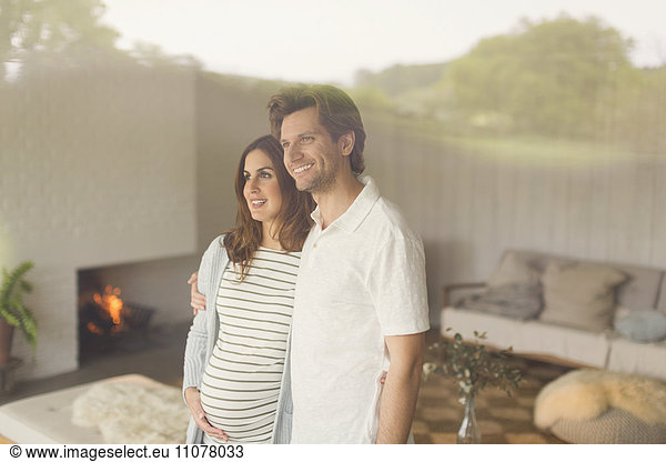 Smiling pregnant couple looking out living room window