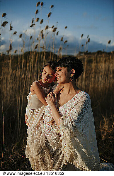Smiling pregnant woman carrying daughter standing in field at sunset