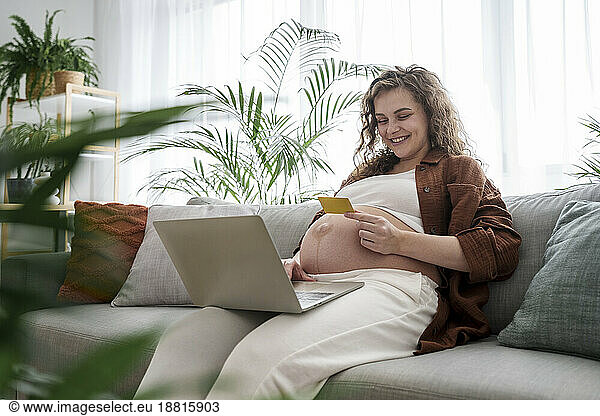 Smiling pregnant woman doing online shopping through credit card at home