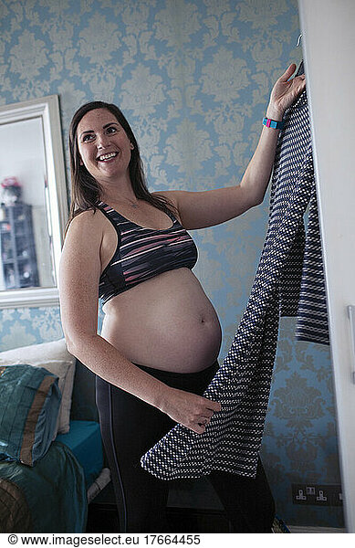 Smiling pregnant woman getting dressed in bedroom
