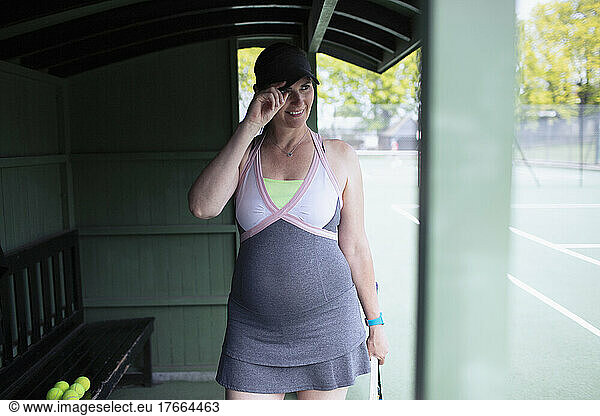 Smiling pregnant woman in dress on tennis court