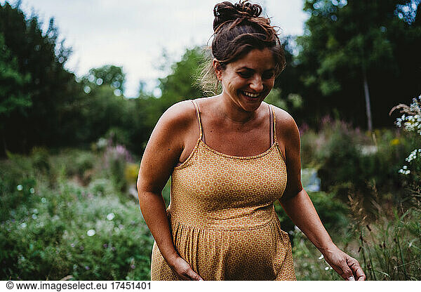 Smiling pregnant woman outside in nature wearing a yellow dress
