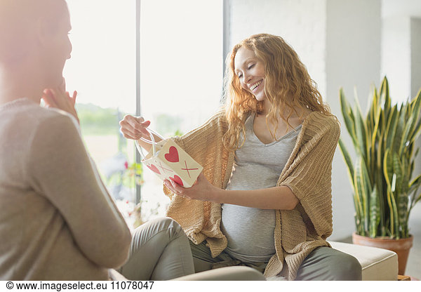 Smiling pregnant woman receiving gift from friend