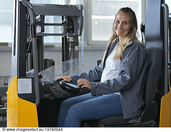 Smiling pregnant woman sitting in forklift at factory