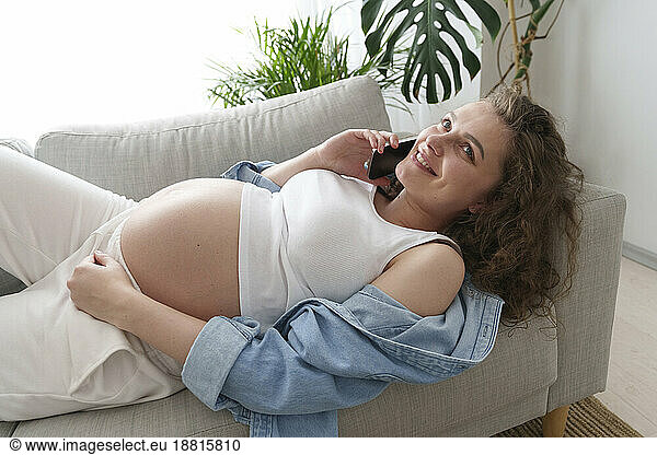 Smiling pregnant woman talking through mobile phone at home