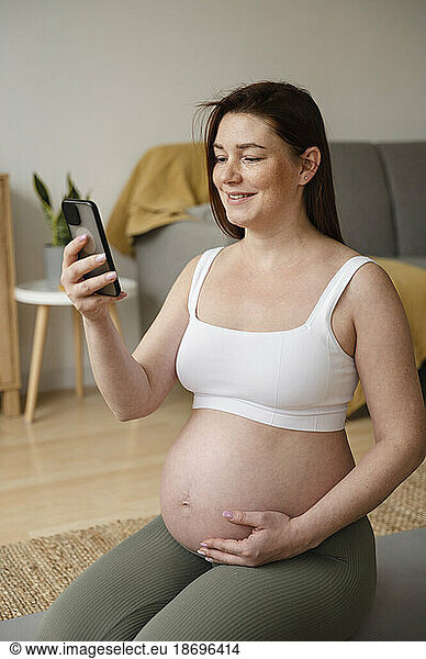Smiling pregnant woman using smart phone sitting at home