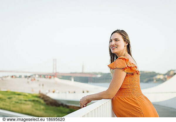 Smiling pregnant woman wearing orange dress leaning on railing