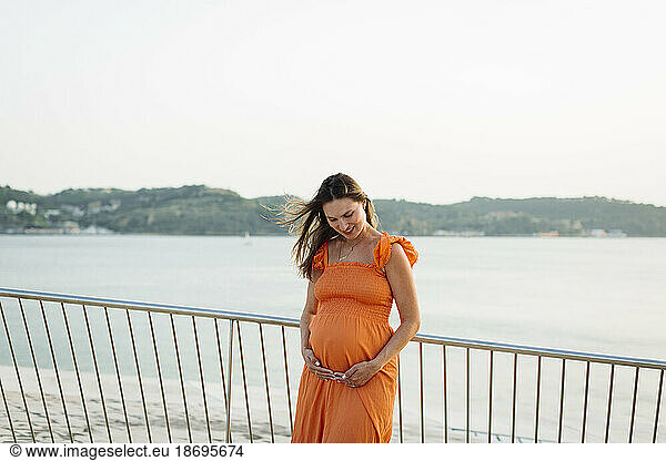 Smiling pregnant woman with hands on stomach by railing