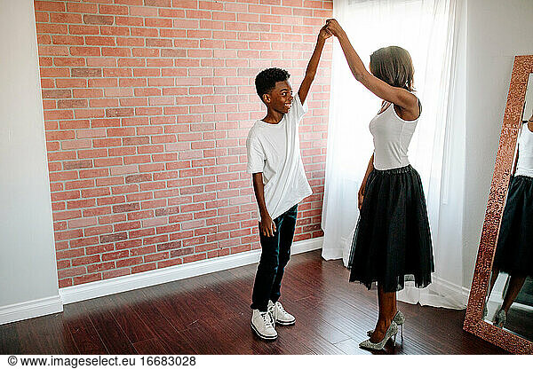 Smiling preteen black boy dancing with pretty mom in sparkly heels