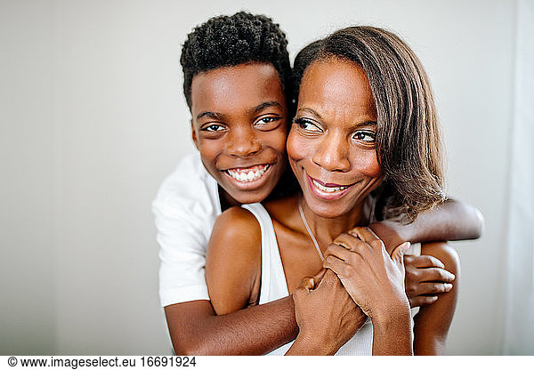 Smiling preteen black boy hugging pretty mom from behind