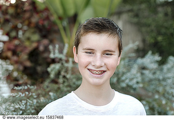 Smiling preteen boy with braces in white tshirt with lush plants
