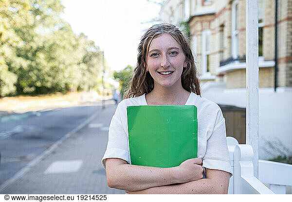Smiling real estate agent holding file folder and standing on footpath
