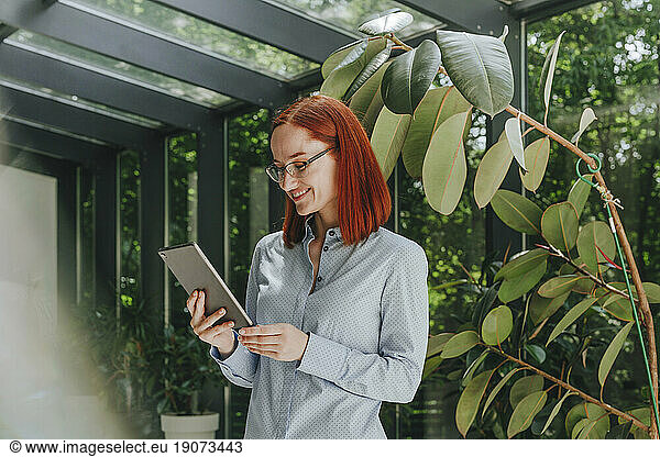 Smiling redhead businesswoman wearing eyeglasses using tablet PC