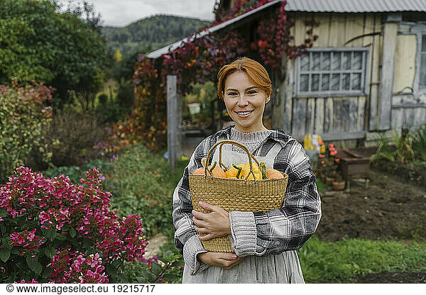 Smiling redhead farmer carrying basket of pumpkins at farm