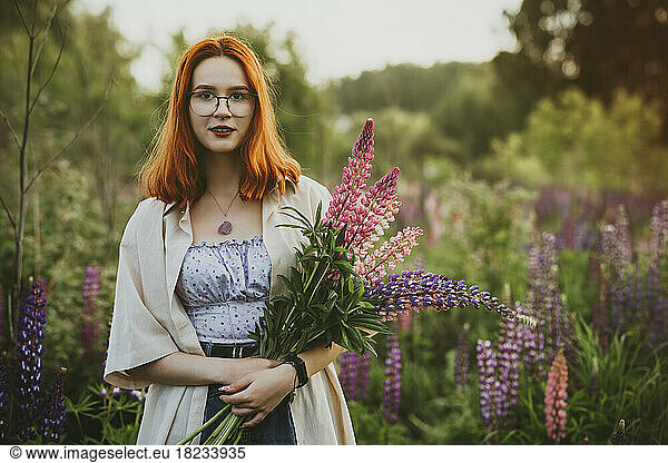 Smiling redhead teenage girl standing with lupin flowers