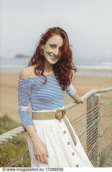 Smiling redhead woman leaning on railing at pier