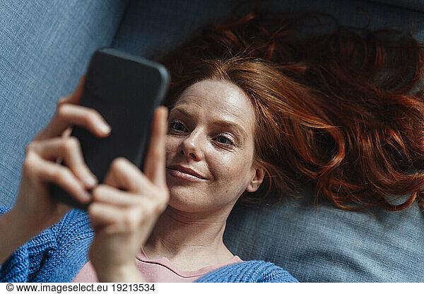 Smiling redhead woman using smart phone on sofa