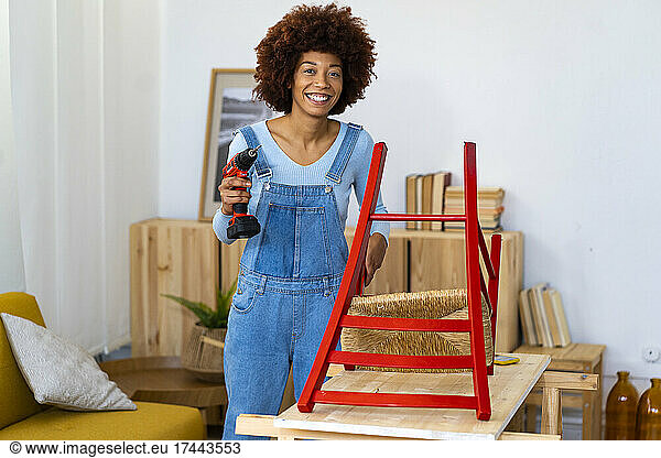 Smiling redhead woman with electric screwdriver standing at table