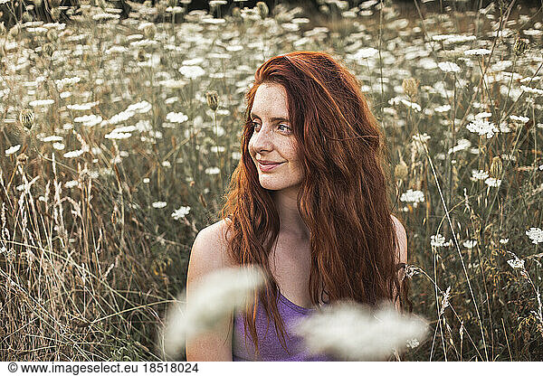 Smiling redhead young woman amidst white flowers in field