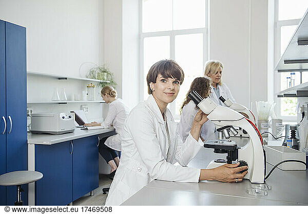 Smiling researcher with microscope at desk