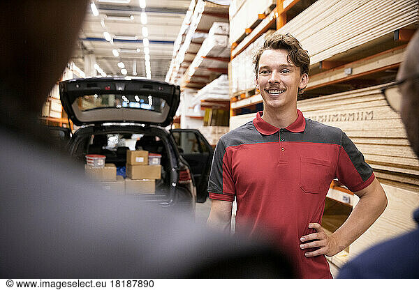 Smiling salesman with hand on hip talking with customer at hardware store