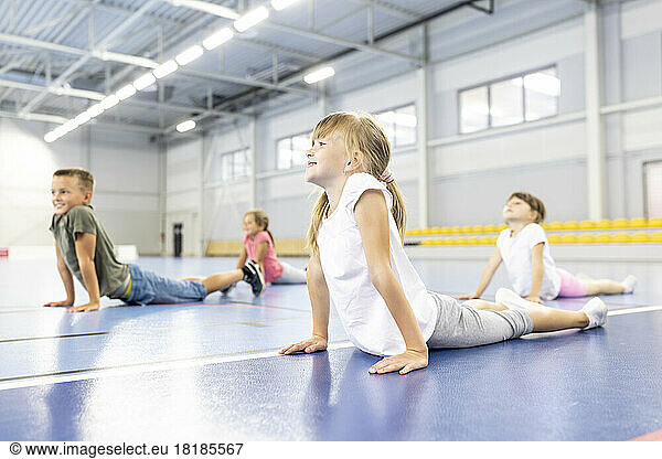 Smiling schoolgirl stretching with friends at sports court