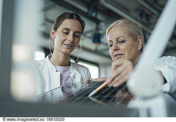 Smiling scientist with colleague discussing over solar panel