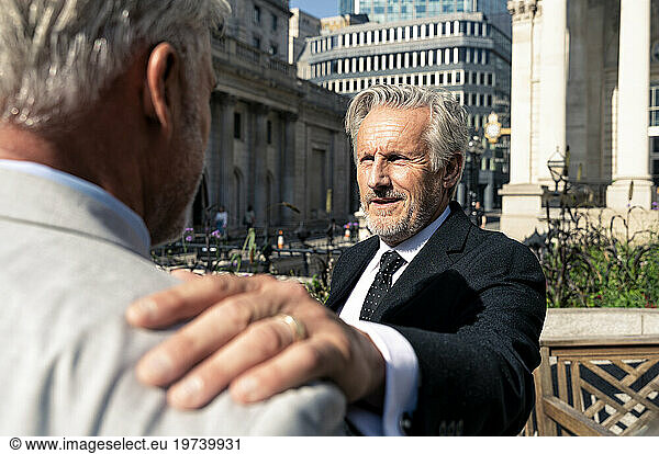 Smiling senior businessman consoling colleague on sunny day