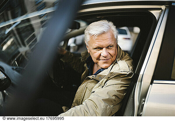 Smiling senior businessman opening door while disembarking from car