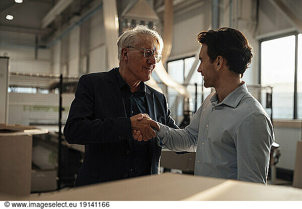 Smiling senior businessman shaking hands with colleague at industry