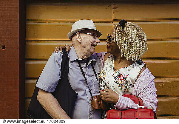 Smiling senior couple with arms around against wall