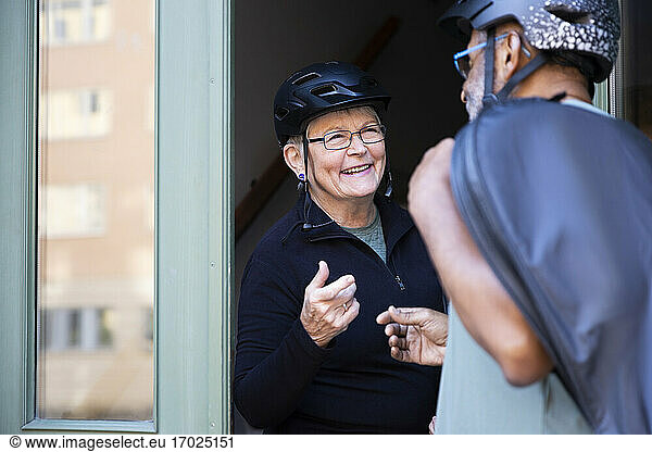 Smiling senior couple with cycling helmet on doorway at home