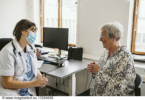 Smiling senior female patient talking with medical expert wearing face mask