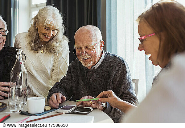 Smiling senior friends using smart phone at table in nursing home