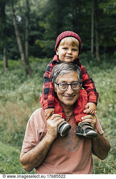 Smiling senior man carrying grandson on shoulders