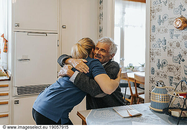 Smiling senior man embracing female caregiver at home