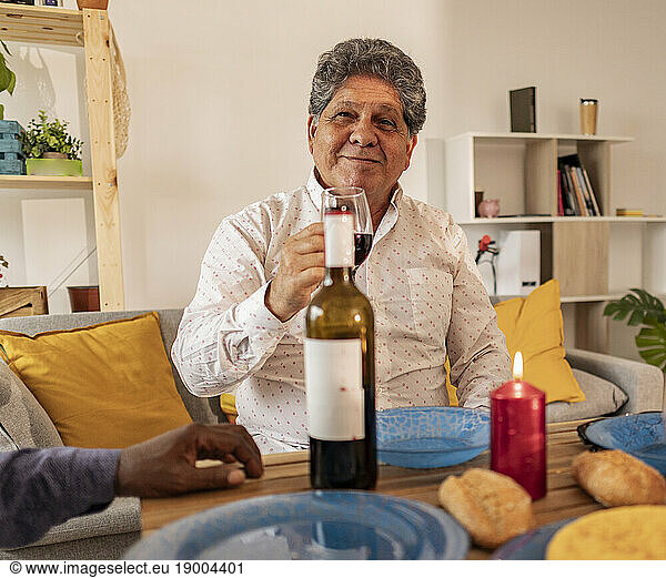 Smiling senior man holding wineglass sitting at dining table