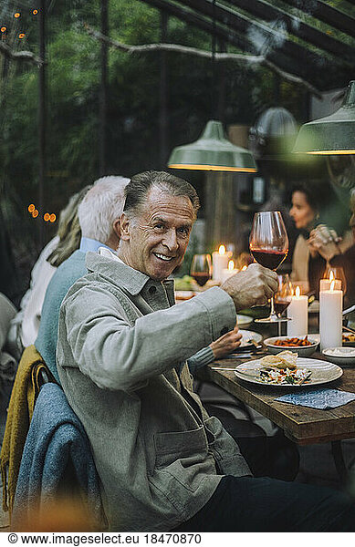 Smiling senior man holding wineglass while sitting at dining table during party