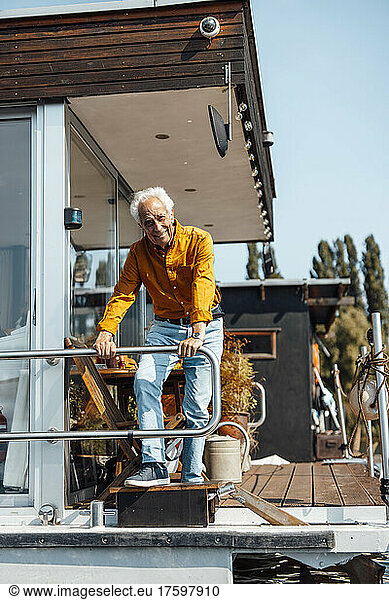 Smiling senior man leaning on railing standing at houseboat