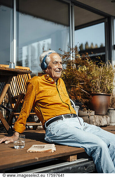 Smiling senior man listening music through wireless headphones at houseboat on sunny day
