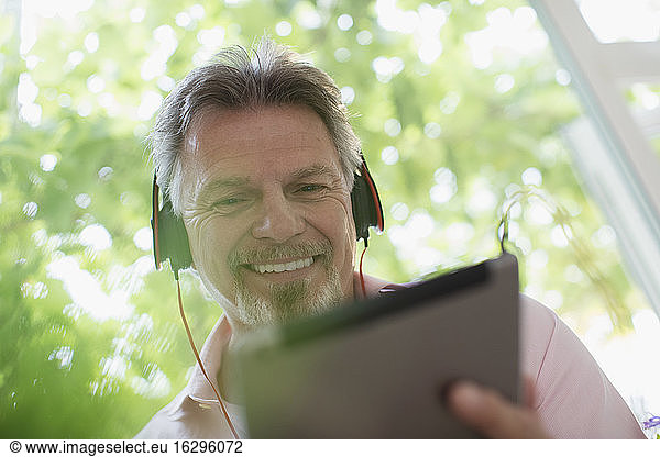 Smiling senior man listening to music with headphones and digital tablet