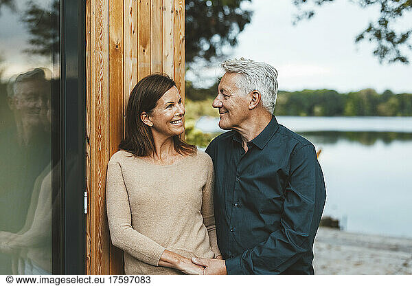Smiling senior man looking at woman standing by wooden wall