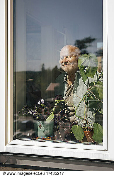 Smiling senior man looking through window on sunny day